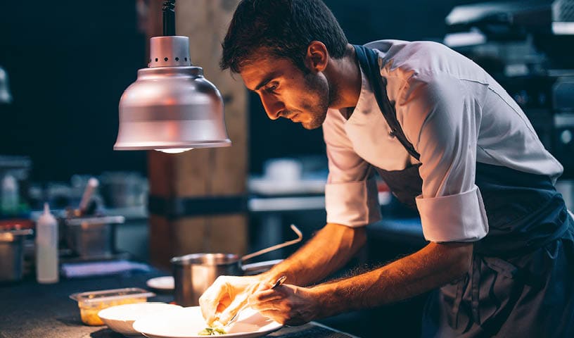 Cook serving food on a plate in the kitchen of a restaurant