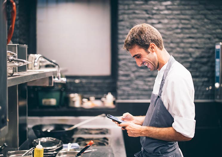 Smiling cook using smartphone in the kitchen of a restaurant