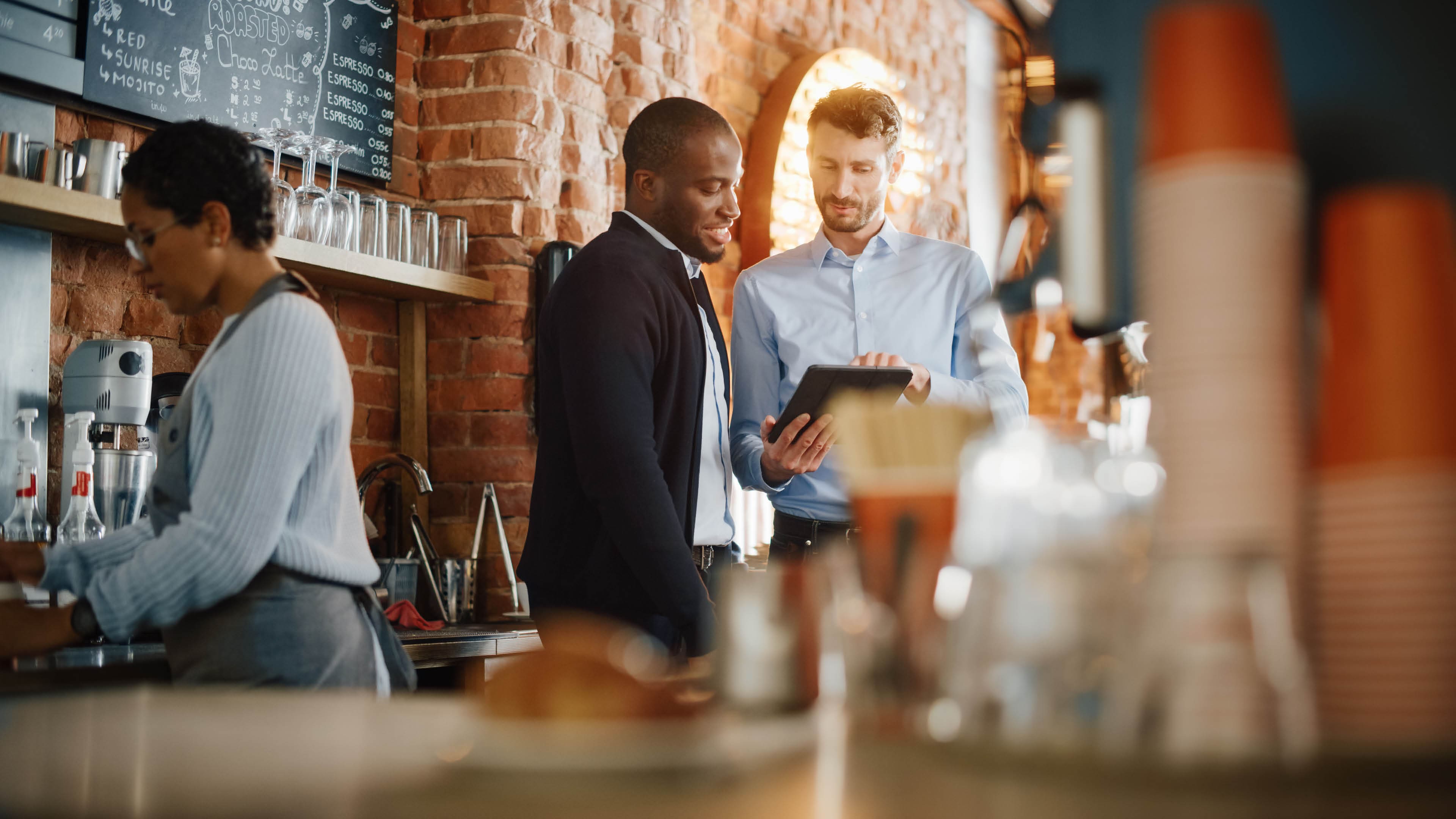 Multicultural Coffee Shop Owners Meeting Behind the Counter and Working on Tablet Computer and Checking Inventory in a Cozy Loft-Style Cafe. Successful Restaurant Managers and Barista at Work.; Shutterstock ID 1882428628; purchase_order: -; job: -; client: -; other: -